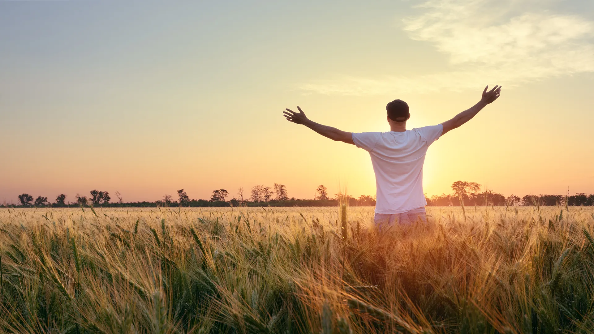 A man standing in a field with his arms open wide at sunset. 