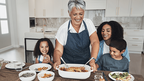 A grandmother prepares a meal with her two grandchildren and daughter