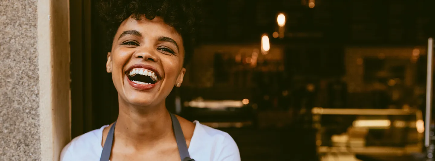 Young African American business owner smiling in front of her shop.