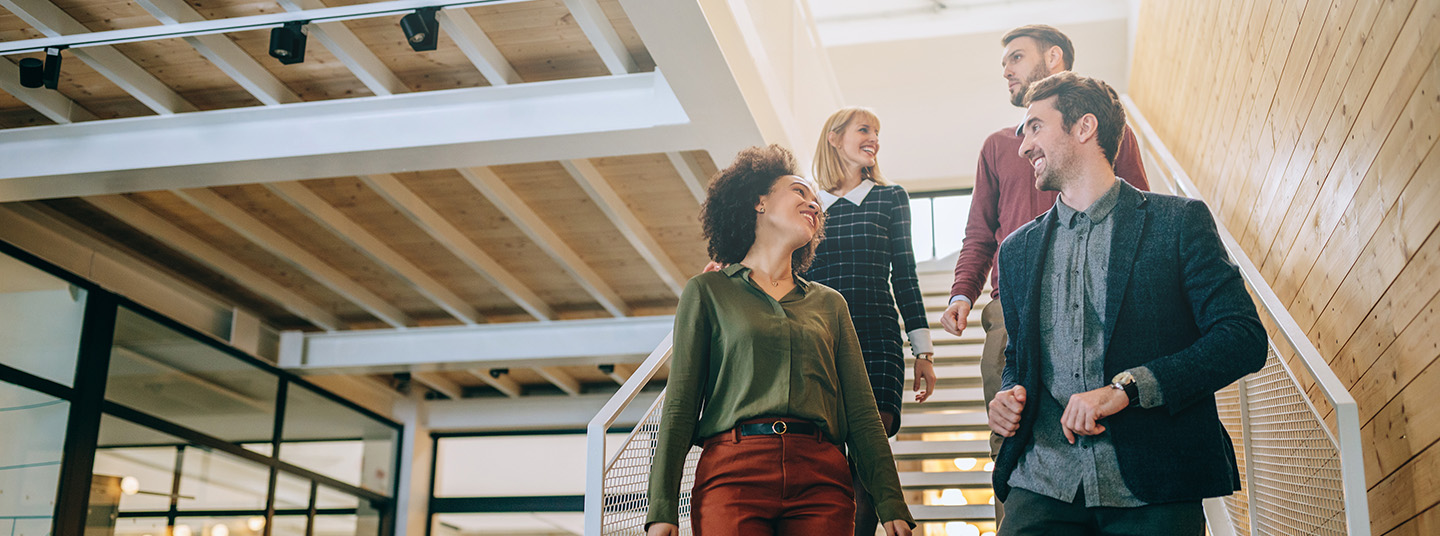 Four employees walking down the interior hallway stairs of their office building