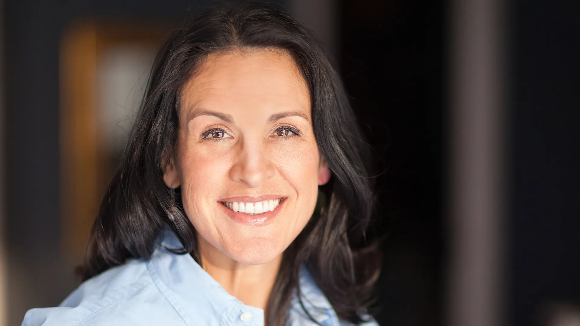 65 year old woman with dark hair smiling at camera.