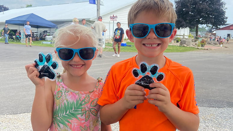 One girl and one boy show off their Everence paw print ice packs and Everence sunglasses on a sunny day at the Elkhart County 4-H Fair.