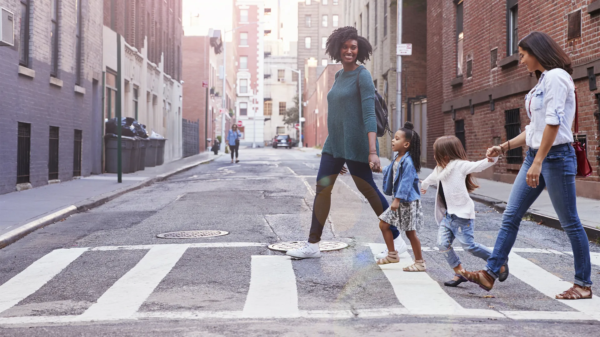 Two women and children walk across a crosswalk in a city while holding hands. 