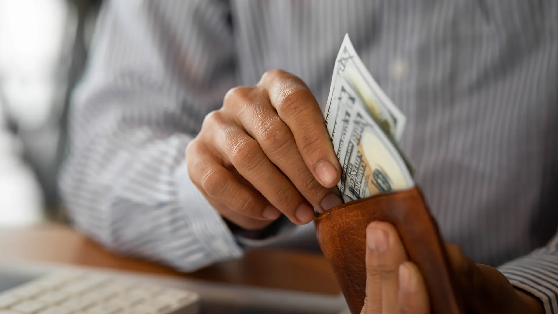 A man puts money in his wallet while sitting over a calculator and a desk.
