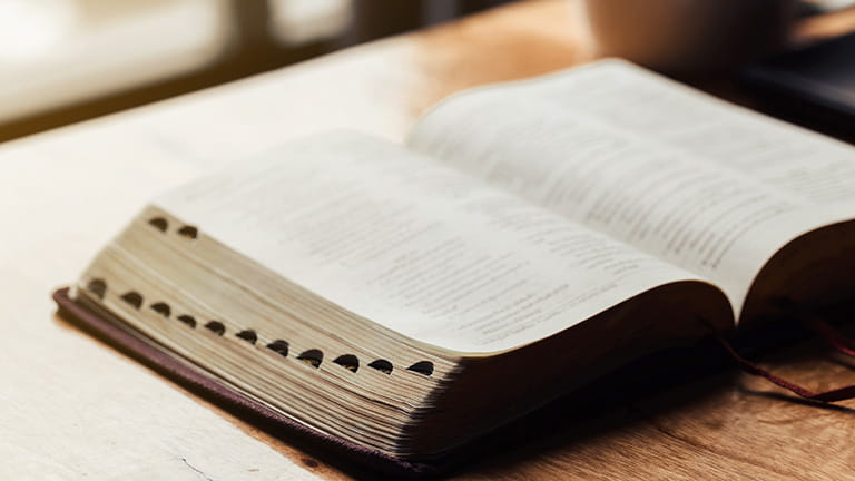 Open bible with a cup of coffee for morning devotion on wooden table