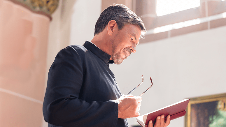 Male pastor in black collared shirt reads his bible in a brightly lit sanctuary