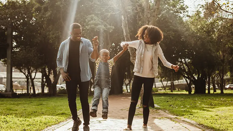 Family swinging their son back-and-forth outside on a sunny day.