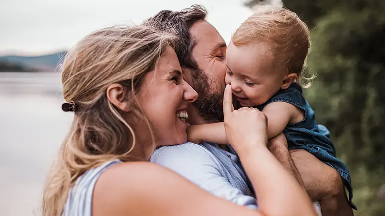 Parents cuddling baby outside by a lake.