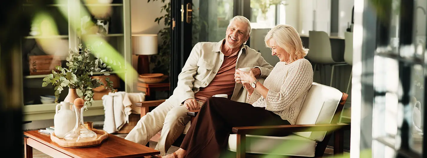 Retirement age couple sitting together on a couch in a clean, green, minimalist room.