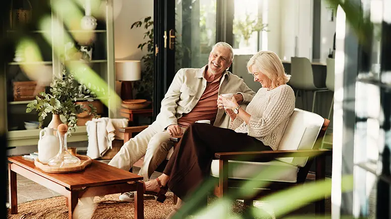 Retirement age couple sitting together on a couch in a clean, green, minimalist room.