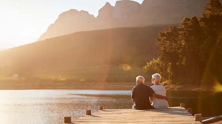 Retirement age couple sitting on a pier looking out over a lake at golden hour.