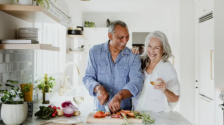Retirement age couple happily cooking in a kitchen together.